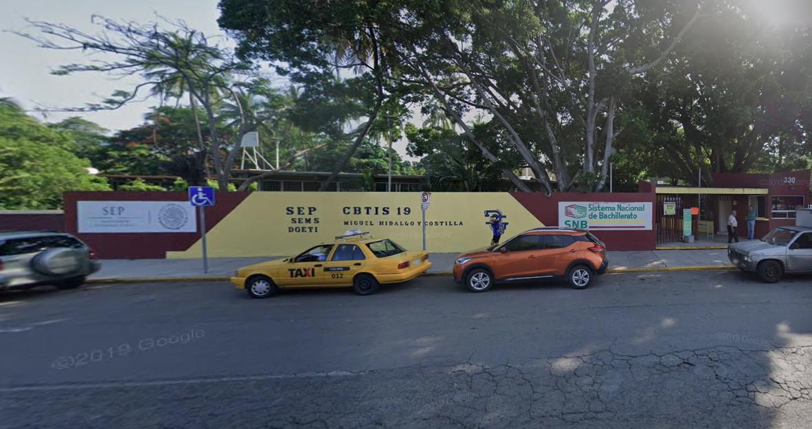 Fotografía en la que se muestra la entrada del plantel, conformada por un muro que combina los colores amarillo y rojo. Sobre el muro, en letras grandes color negro dice Cebetis 19. Al terminar el muro del lado derecho hay una reja color negro que da acceso al plantel.